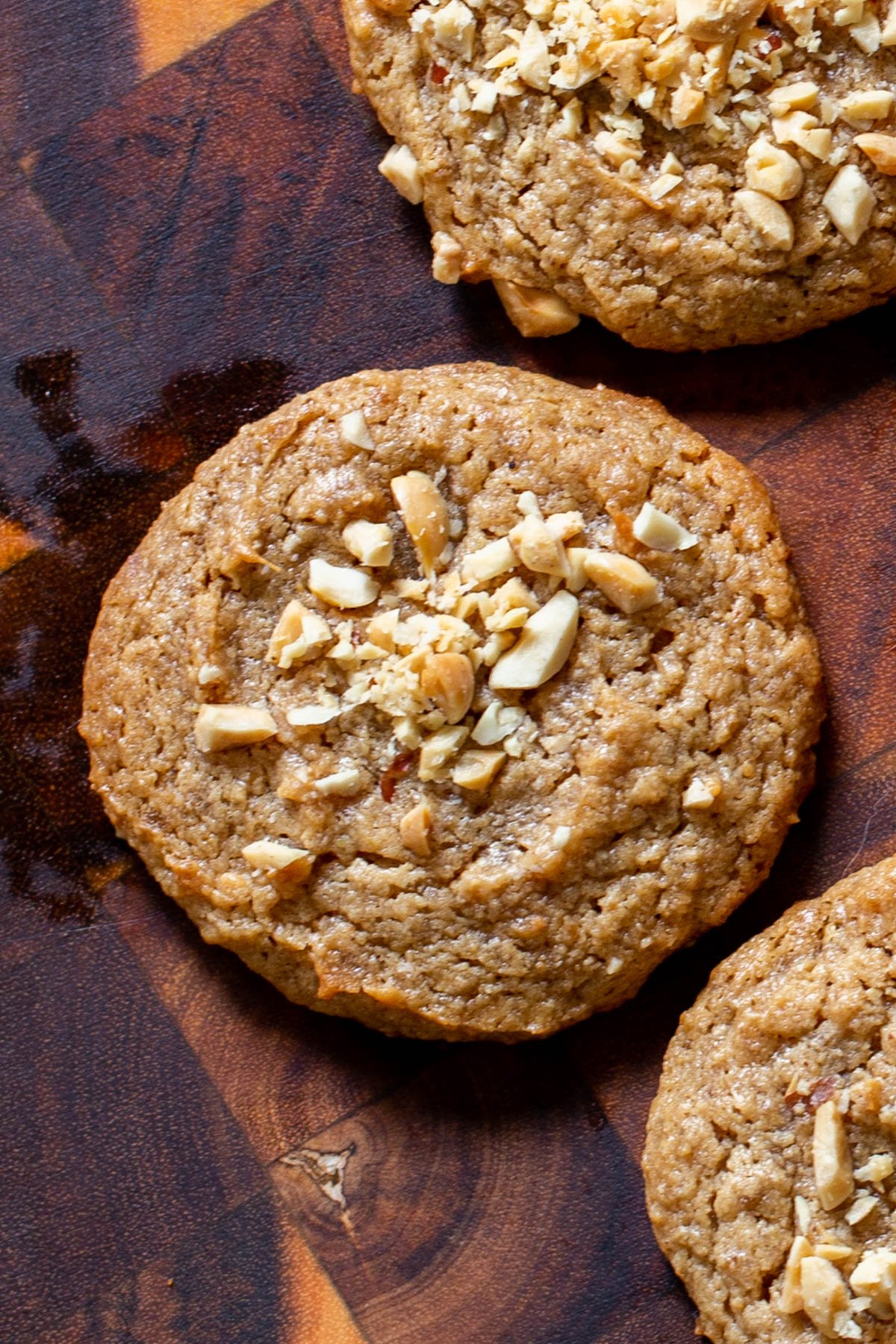 three vegan no flour peanut butter cookies on a wooden board topped with crushed peanuts