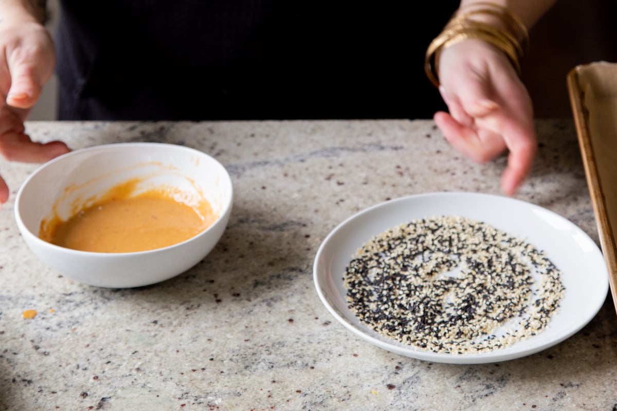 a bowl with vegan peanut sauce and a plate with sesame seeds on. a concrete countertop