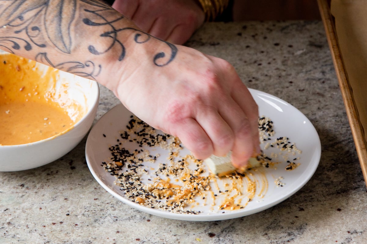 peanut sauce coated chunk of tofu being turned in plate with sesame seeds to make sesame crusted tofu