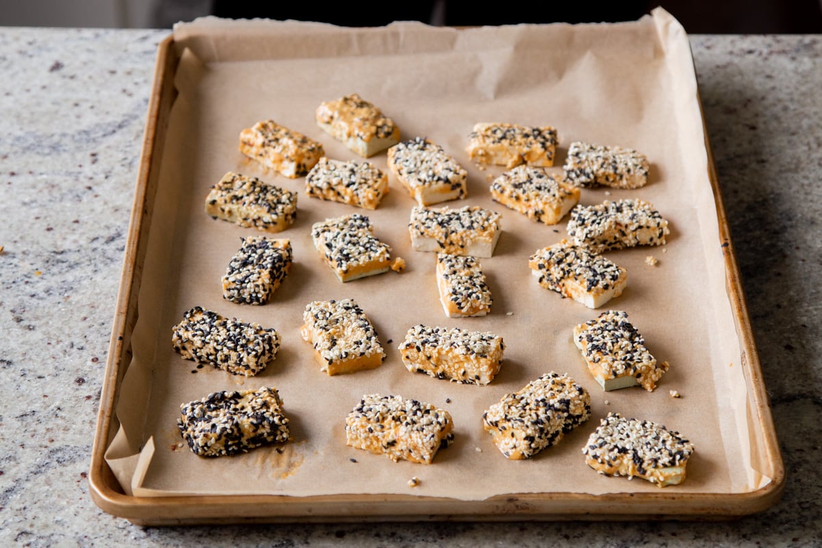 blocks of tofu coated with peanut butter and sesame on a baking sheet