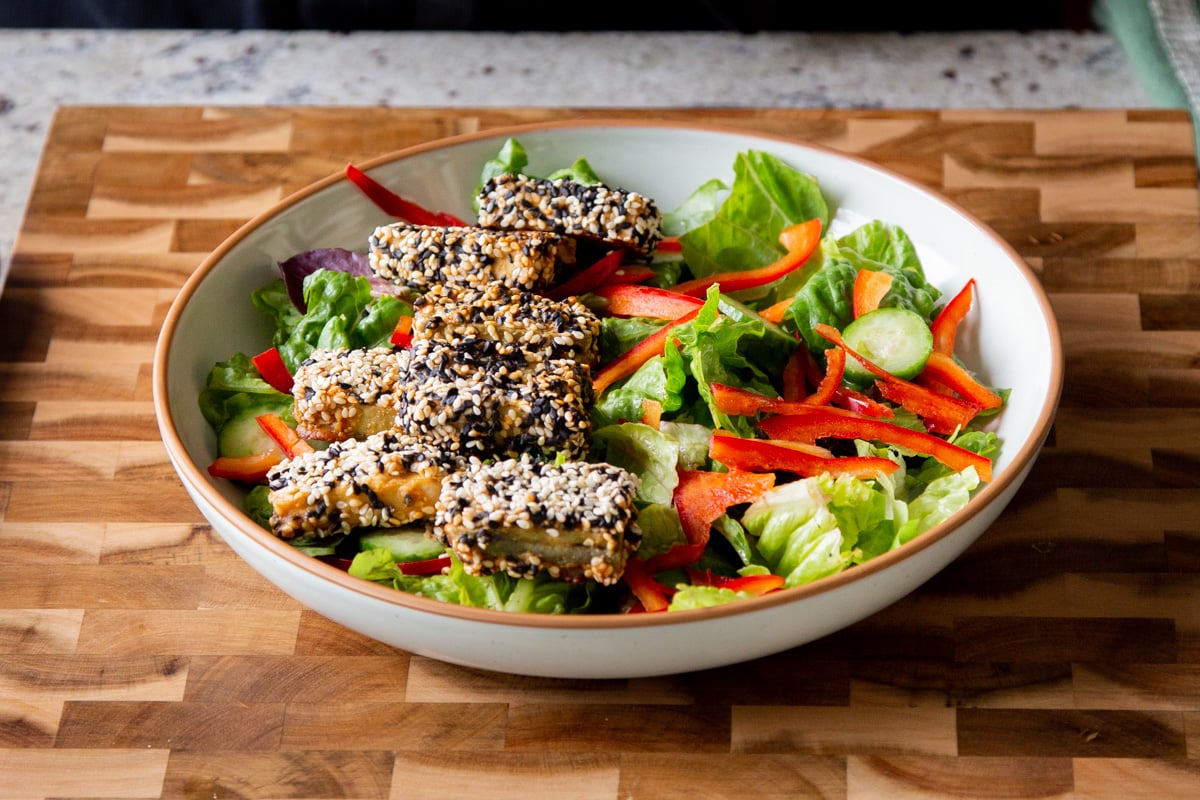 a shallow bowl with greens topped with sesame crusted tofu