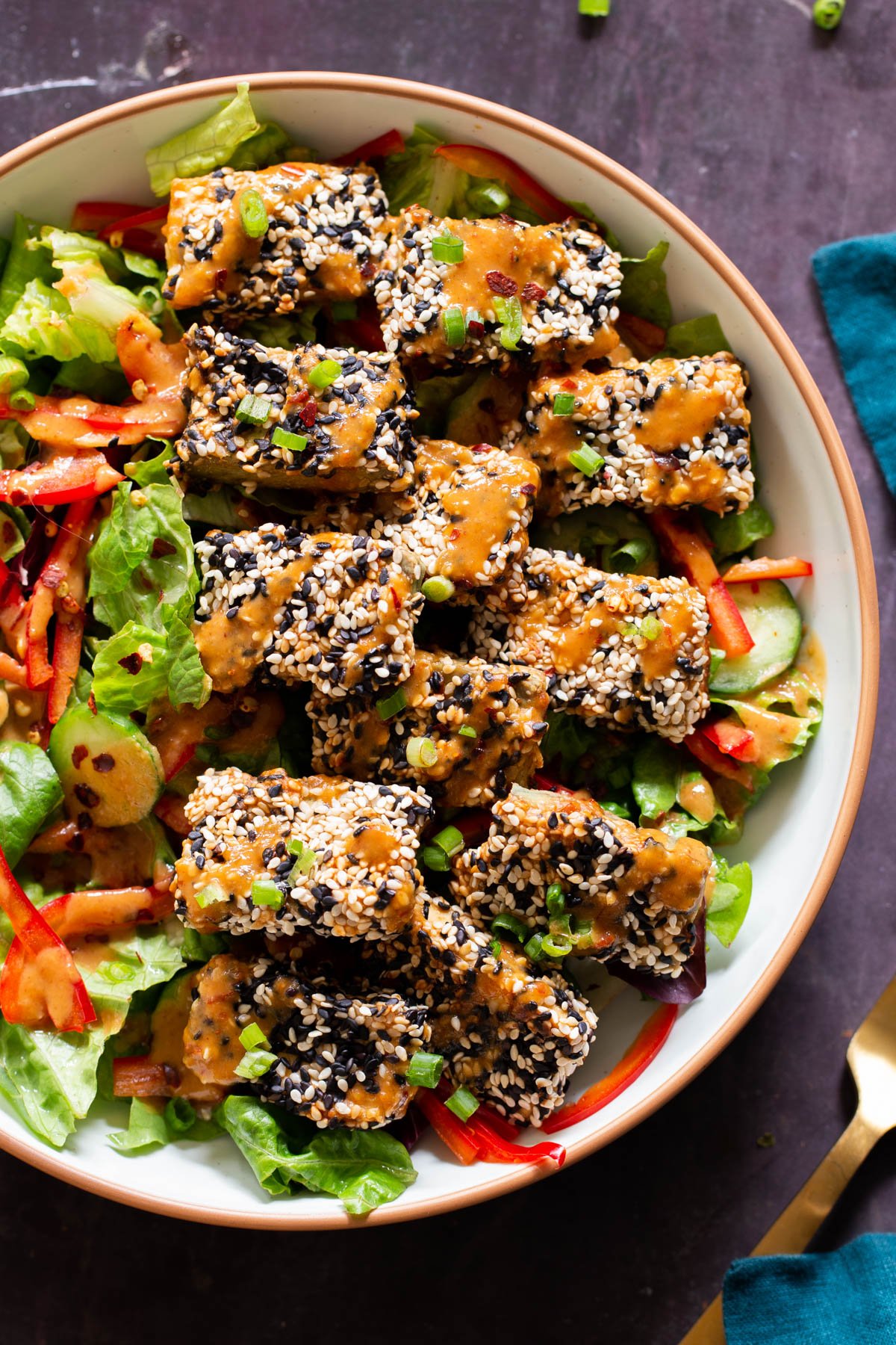 a salad bowl topped with sesame crusted tofu and drizzled with peanut sauce