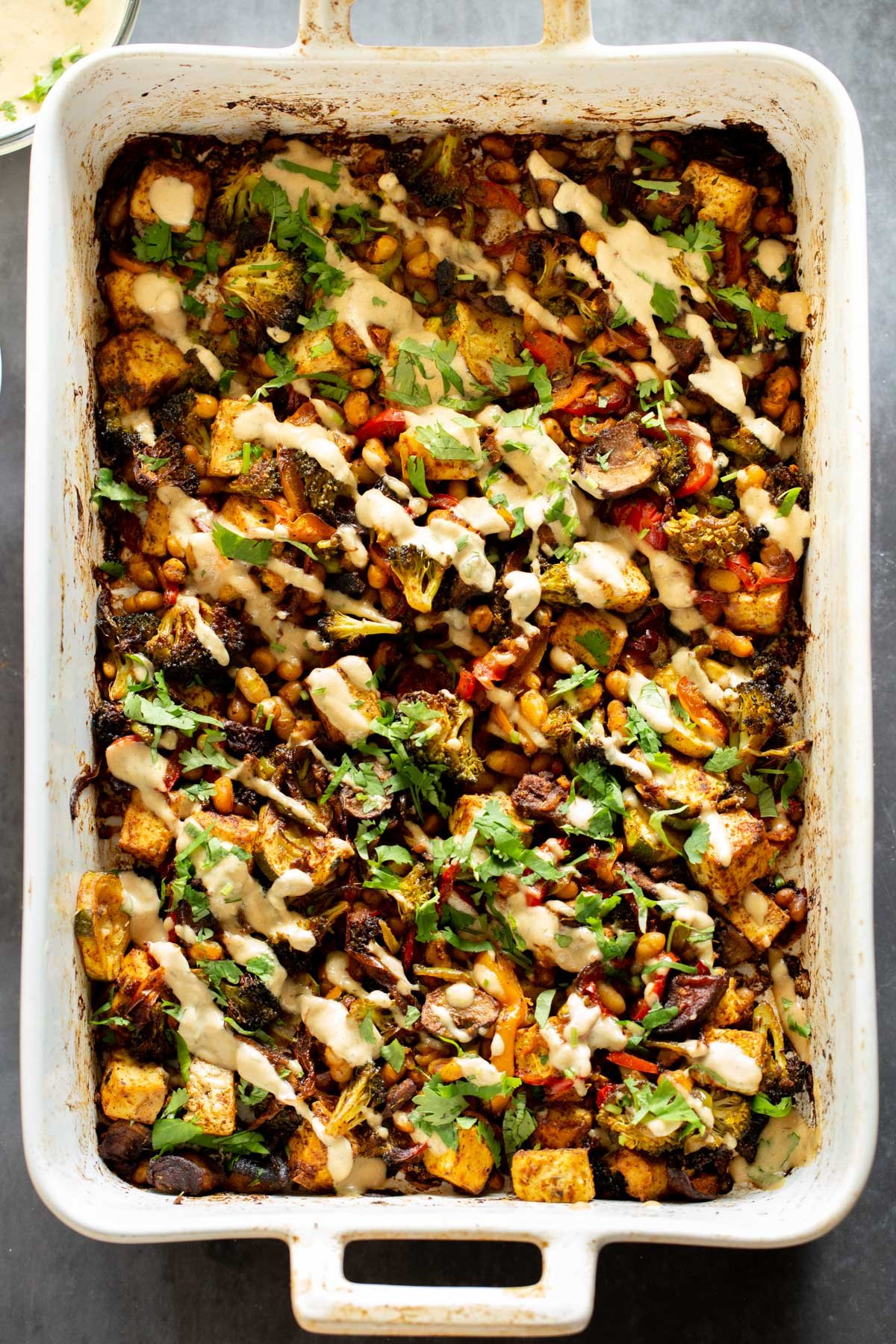 a baking pan with sheet pan veggies drizzled with creamy tahini sauce