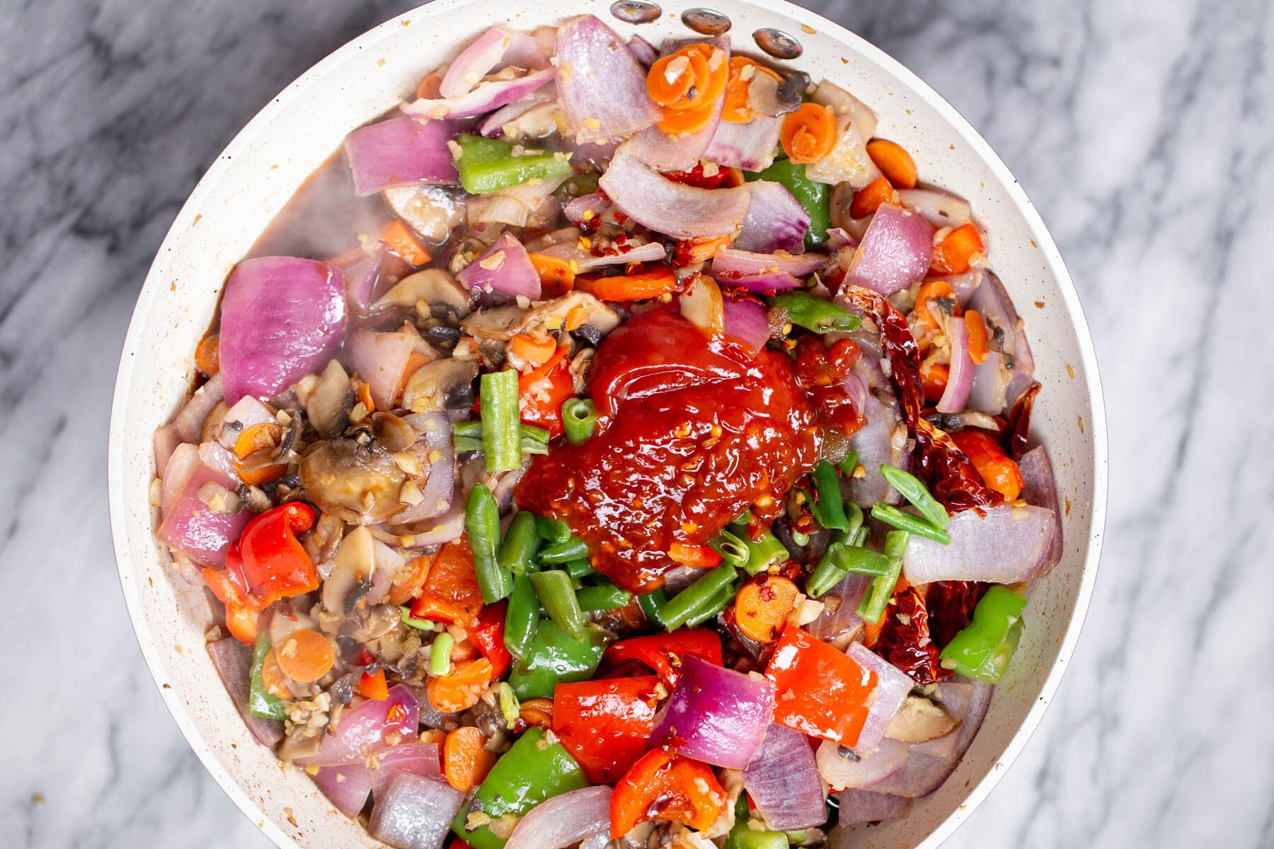 sauce ingredients being added to a frying pan with vegetables