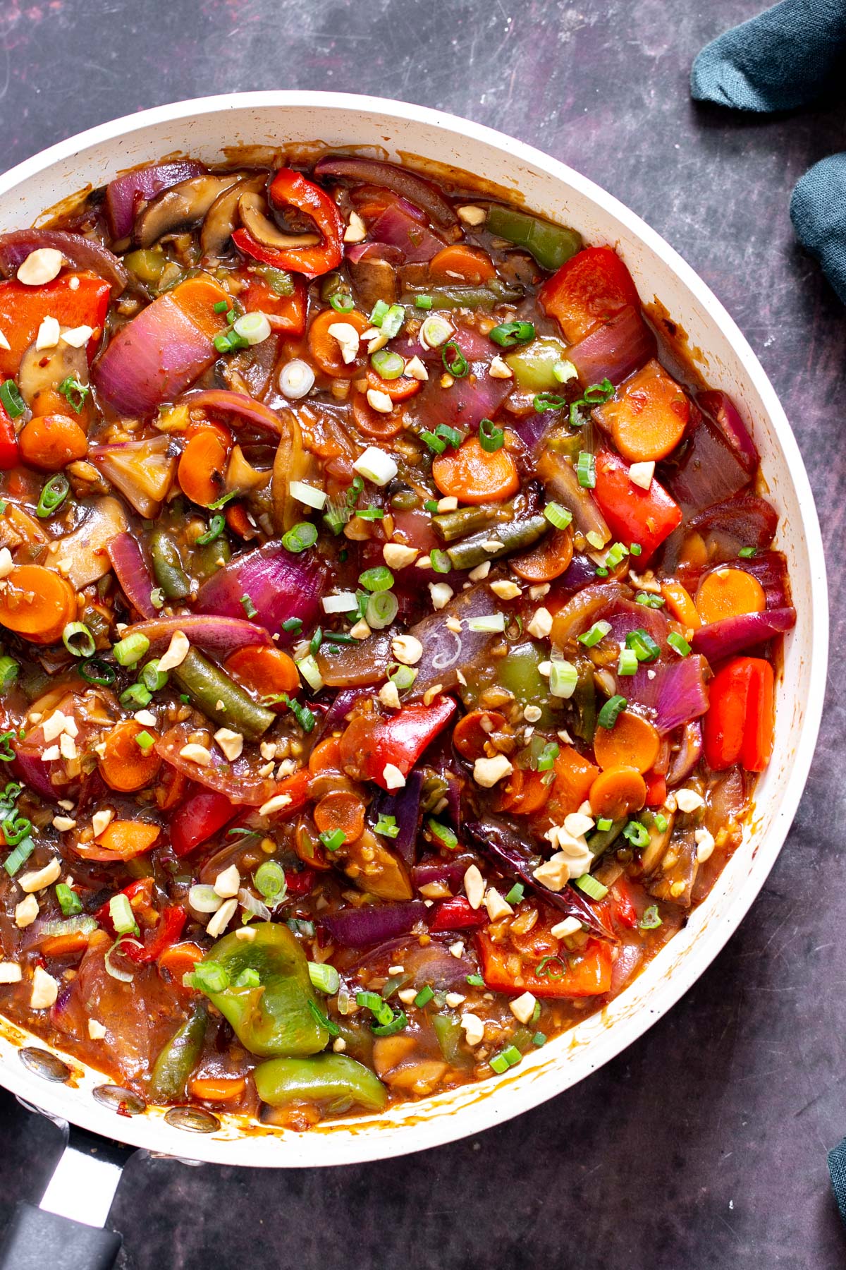 a big white skillet with sweet and sour veggies in hot garlic sauce sprinkled with chopped nuts and green onions