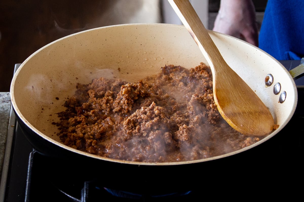 veggie crumbles being sauteed in a frying pan with a wooden spoon
