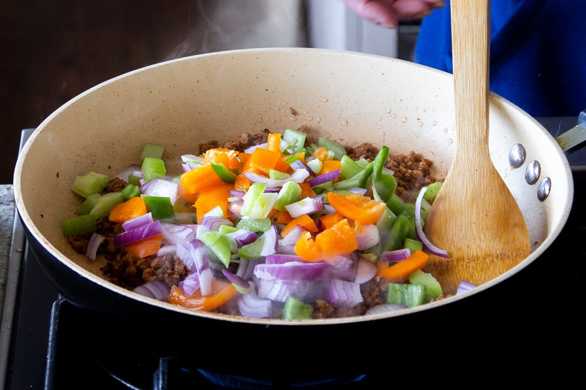 chopped veggies being added to a frying pan with veggie crumbles