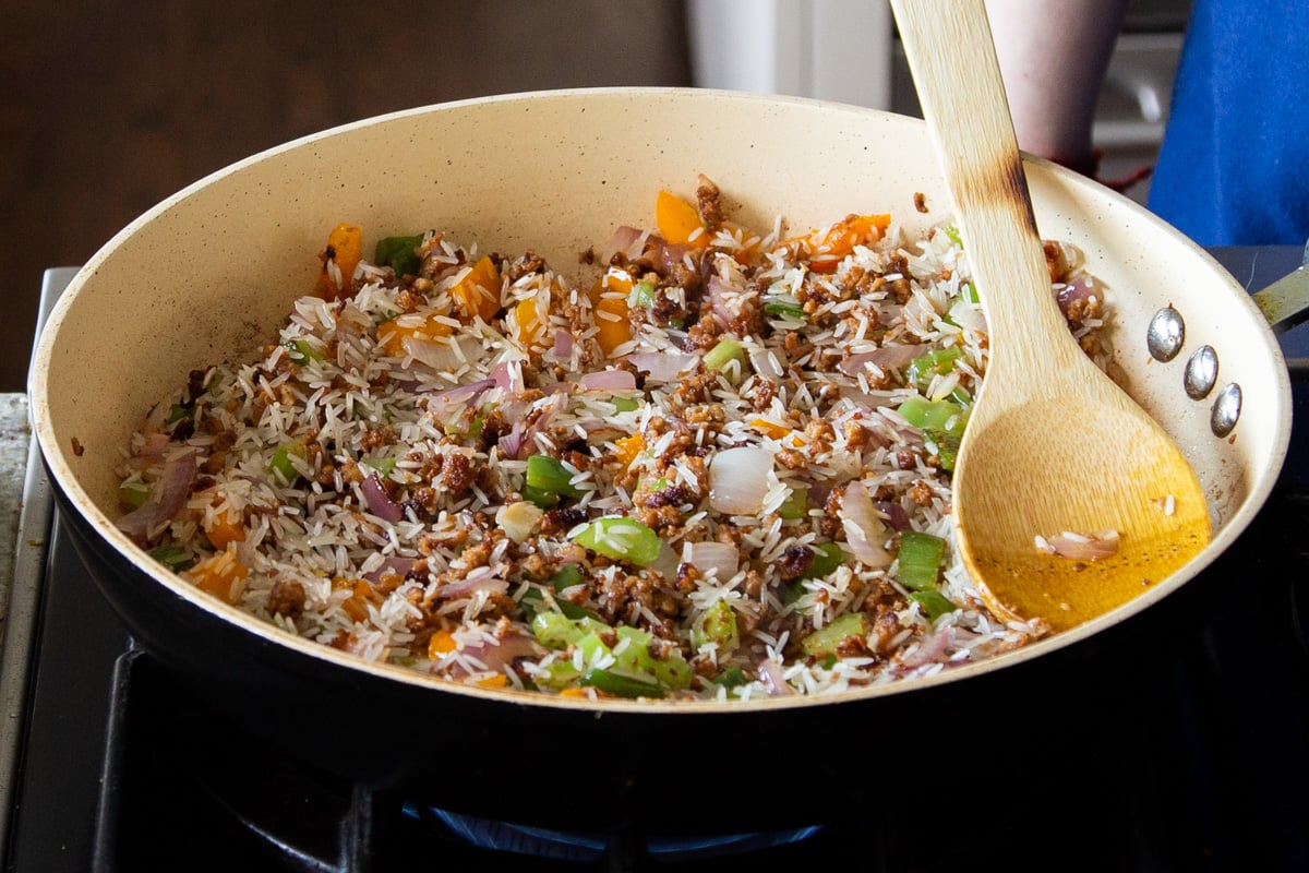 a frying pan with Cajun Dirty Rice with a wooden spoon