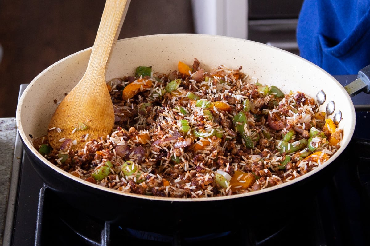 a frying pan with veggies and rice with a wooden spoon on the side