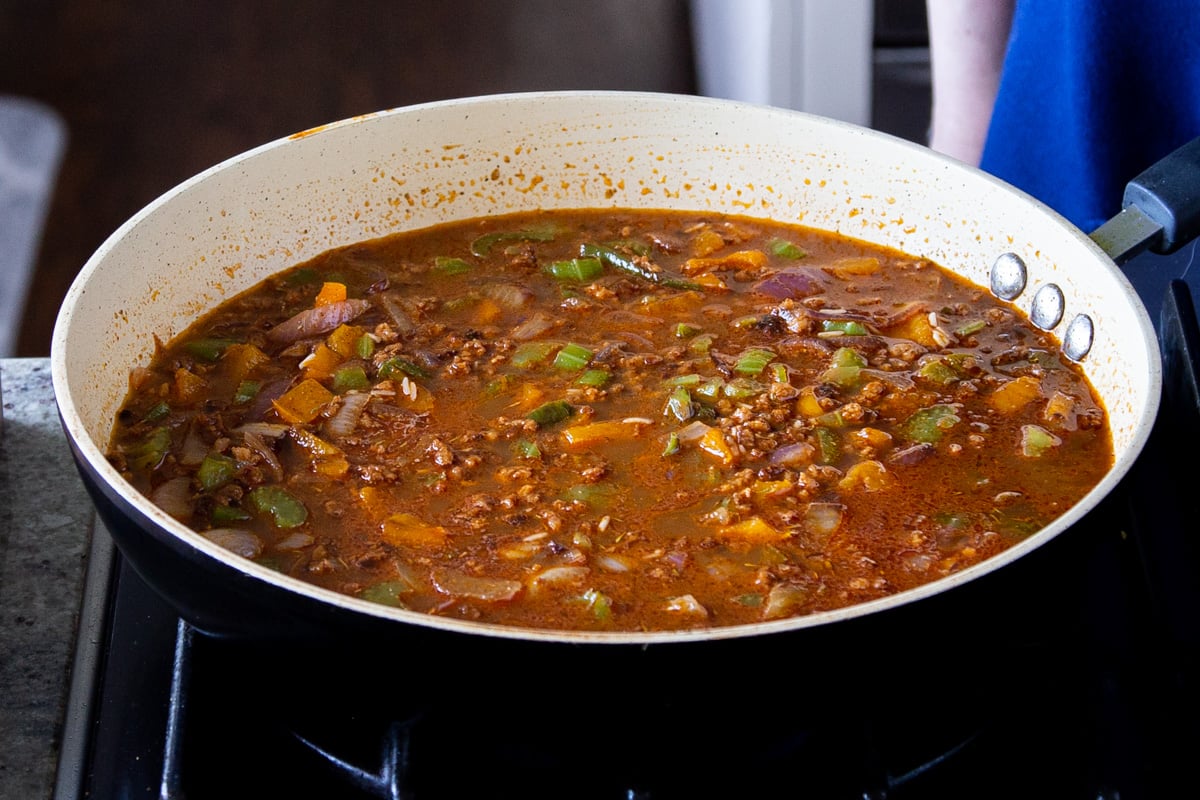 a sauteeing pan with veggies veggie crumbles and added broth on a stovetop