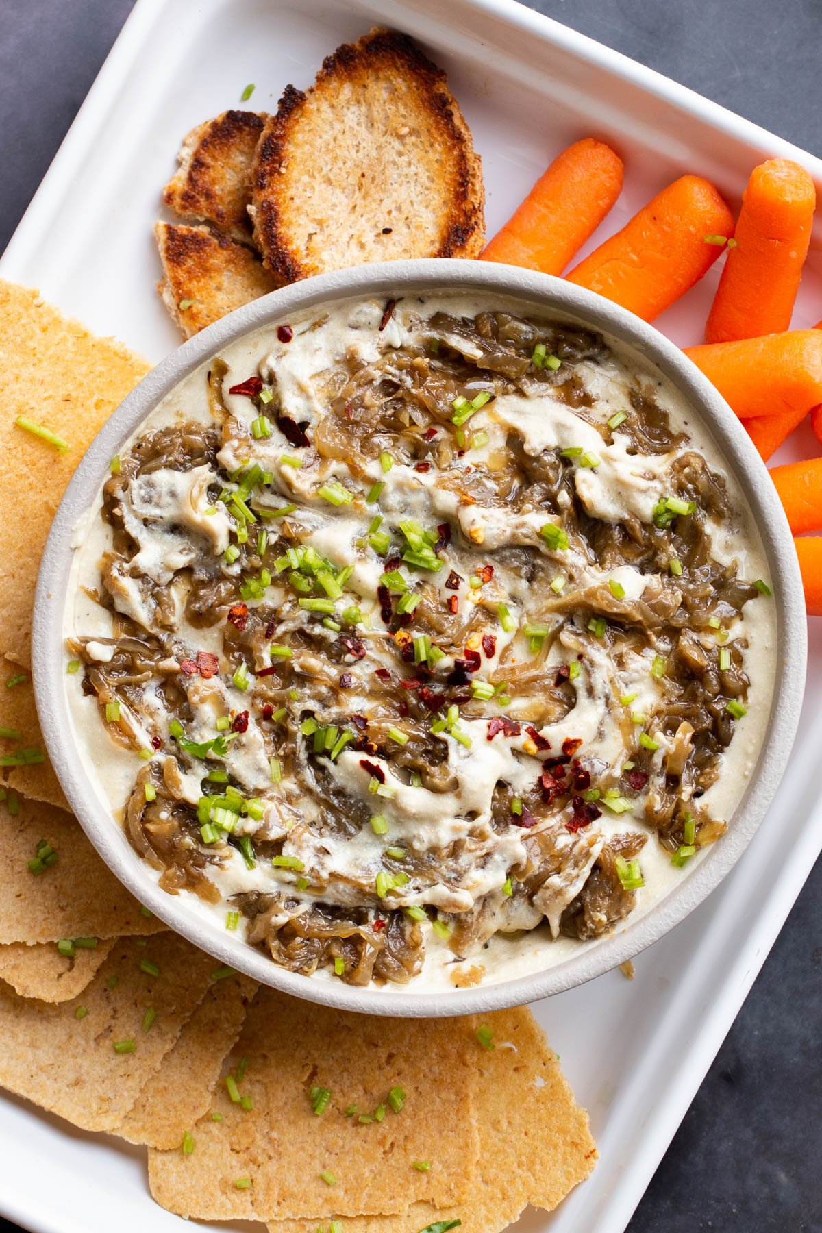 overhead shot of a bowl of vegan French Onion Dip surrounded with veggies and crackers