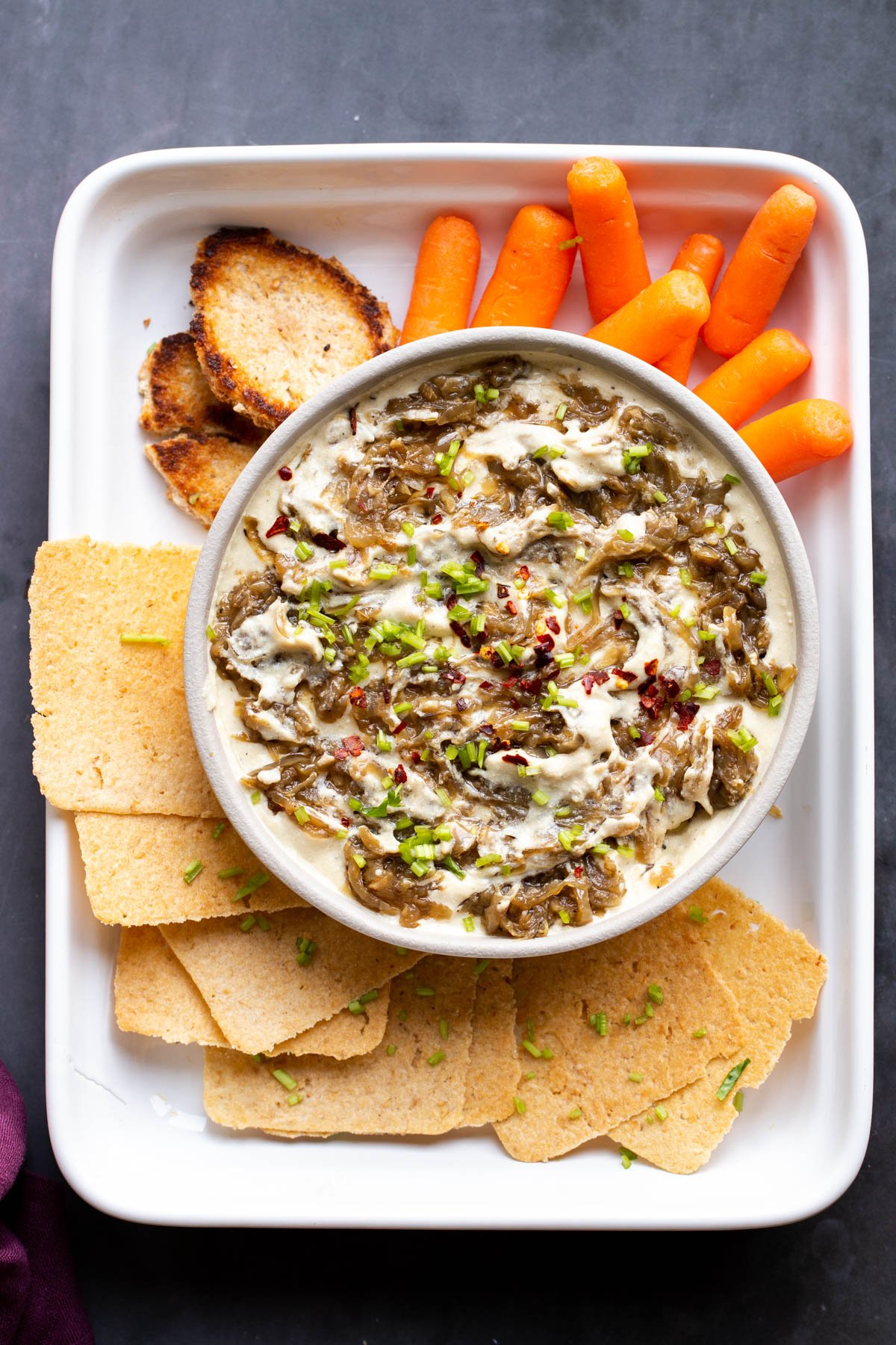 overhead shot of a bowl with vegan caramelized onion dip served with crackers and carrots