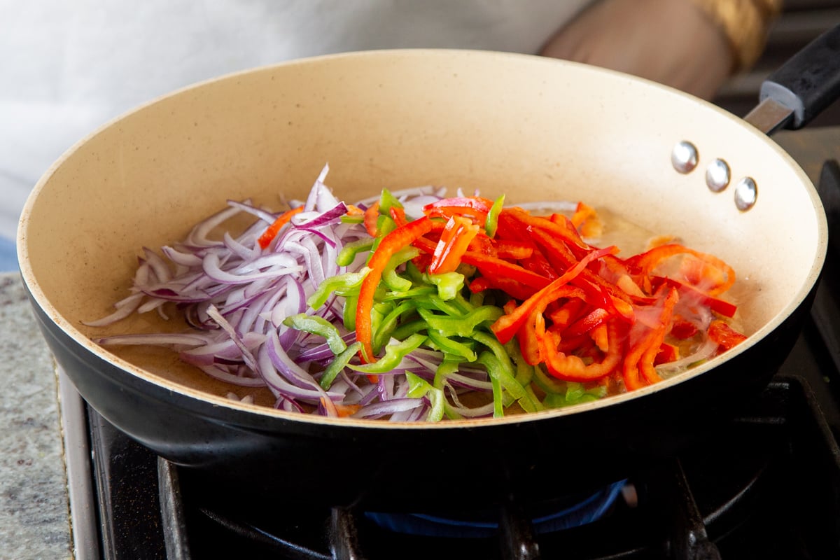 sliced onions and bell peppers being sauteed in a sauteeing pan