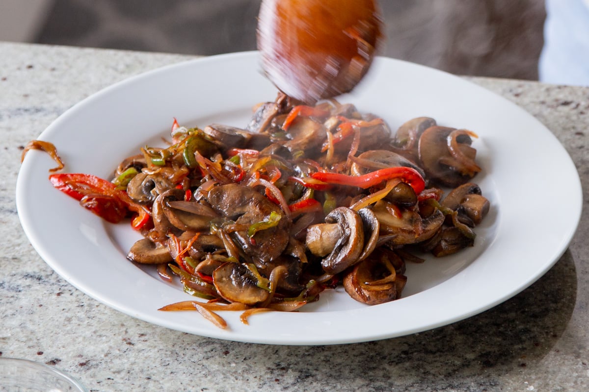 sauteed mushrooms and bell peppers being transferred to a white plate