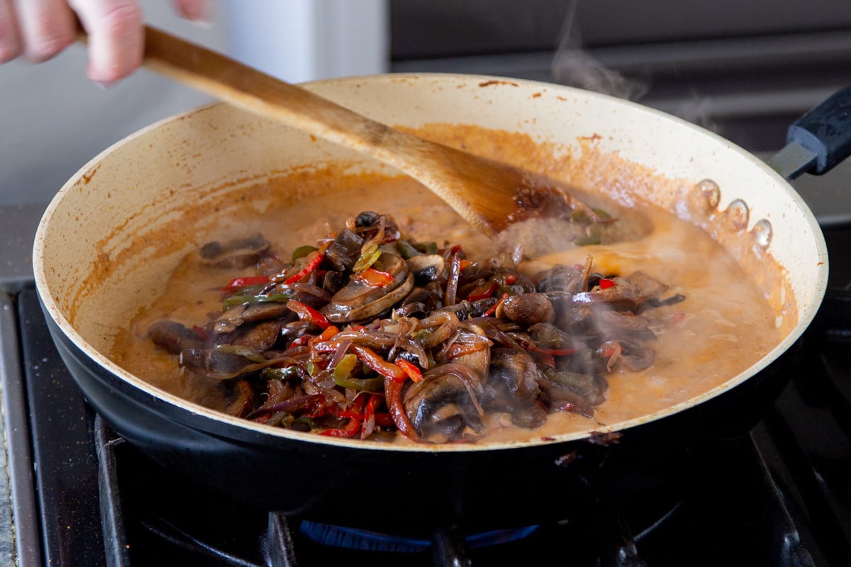 sauuteed mushrooms and bell peppers being added back into the vegan patiala sauce in a saucepan