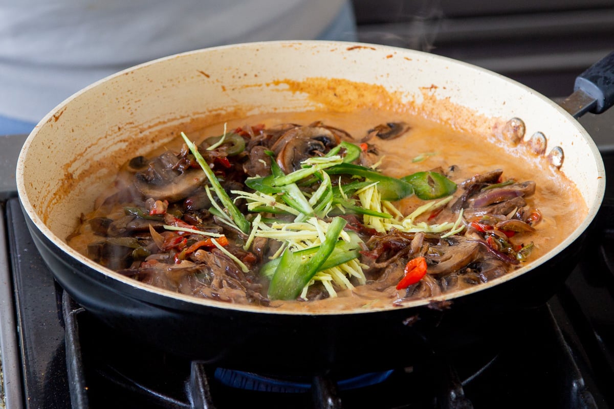 julienned ginger and chili being added to a saucepan with vegan patiala sauce