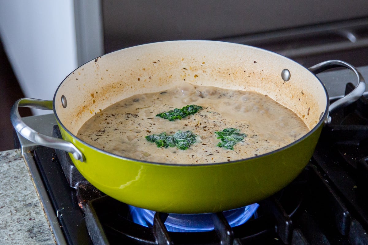 spinach being added to a saucepan with cashew cream