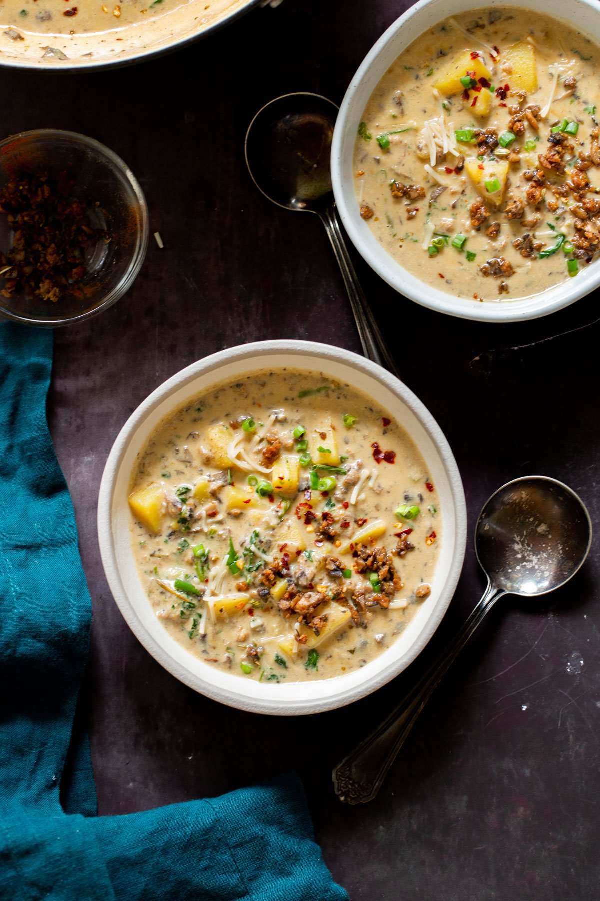 two bowls of vegan zuppa toscana with two silver spoons on the side