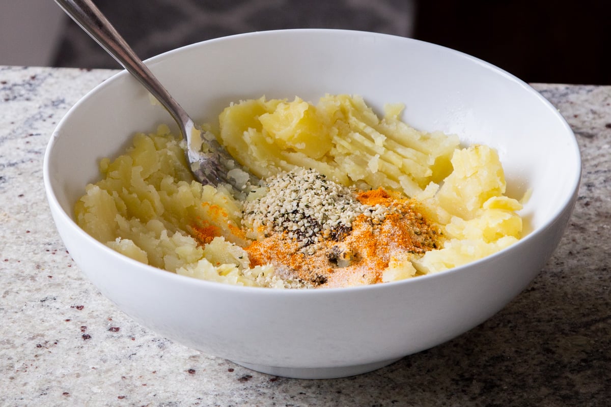 adding seeds and spices to the bowl of mashed potatoes