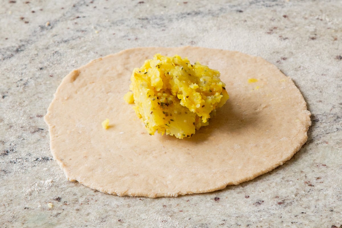 paratha dough rolled out on a lightly oiled countertop with potato filling in a pile in the center