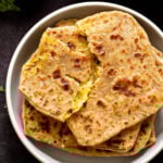 aloo paratha pilled up on a plate, top one is torn open, so you can see the filling