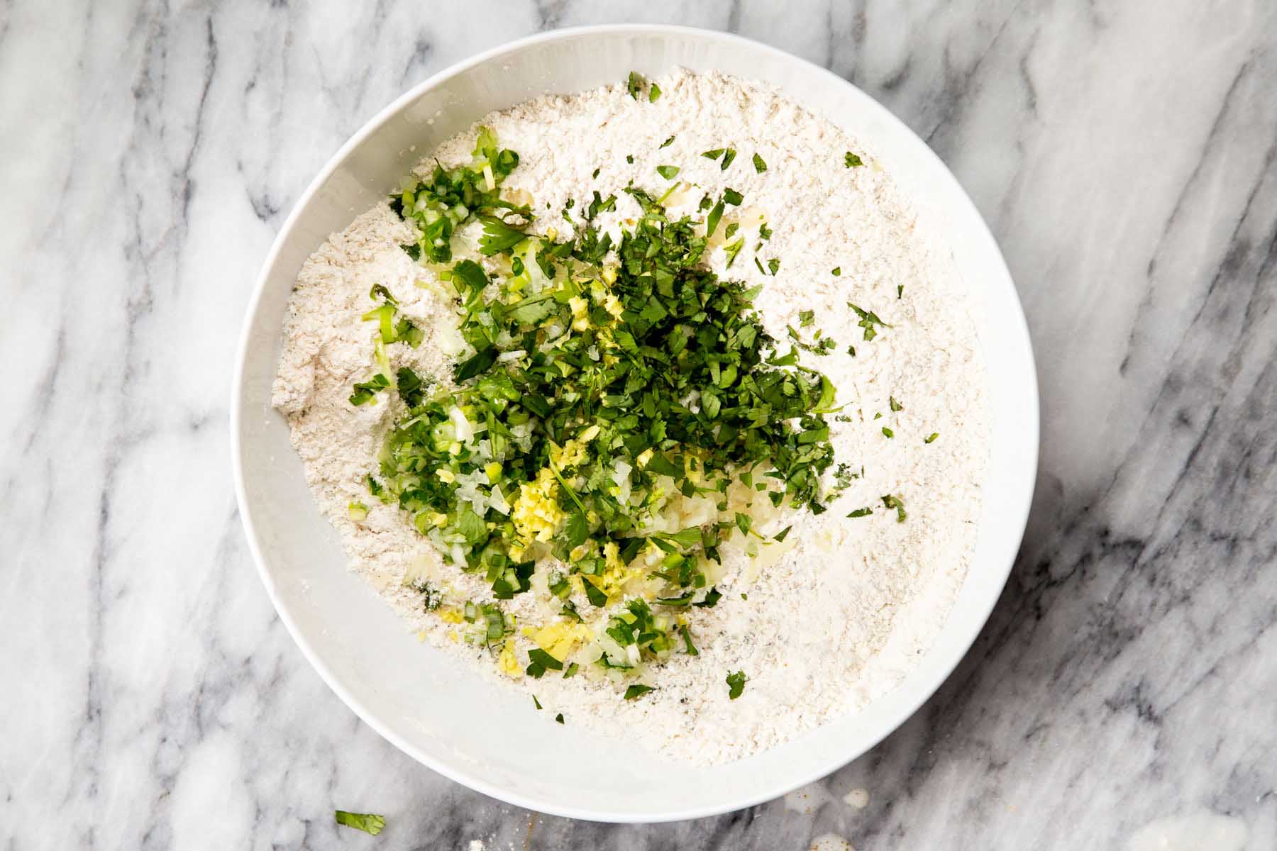 adding herbs to the bowl of flour