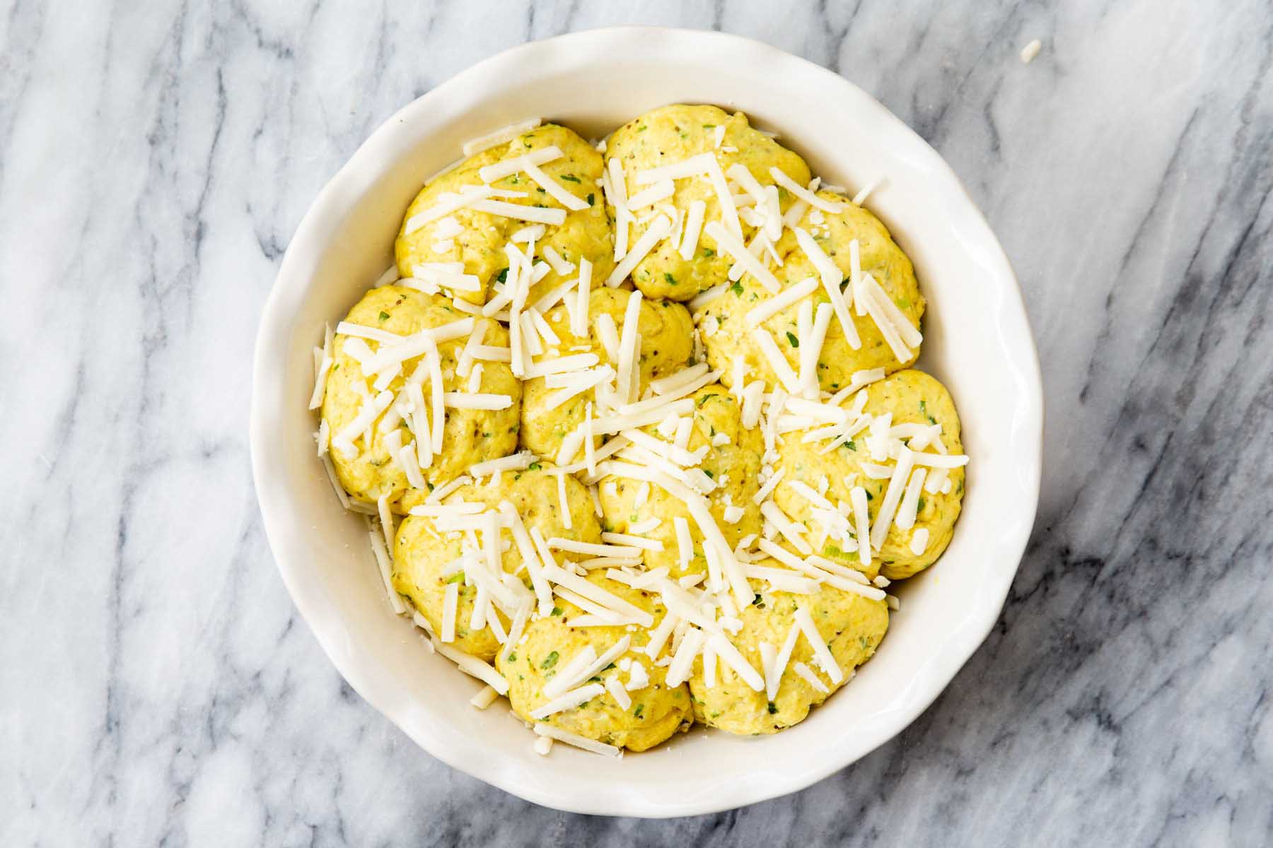 dough balls arranged in a baking dish before baking, cheese added on top