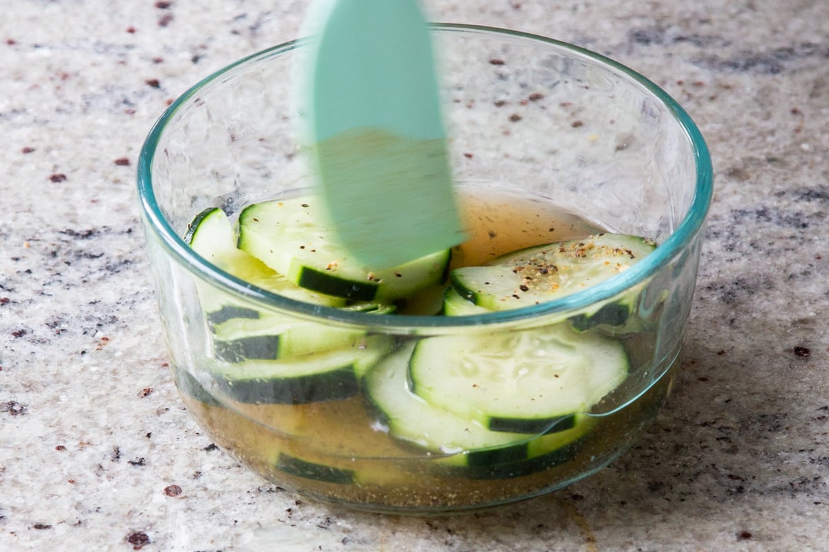 mixing sliced cucumber with homemade pickle brine in a small bowl