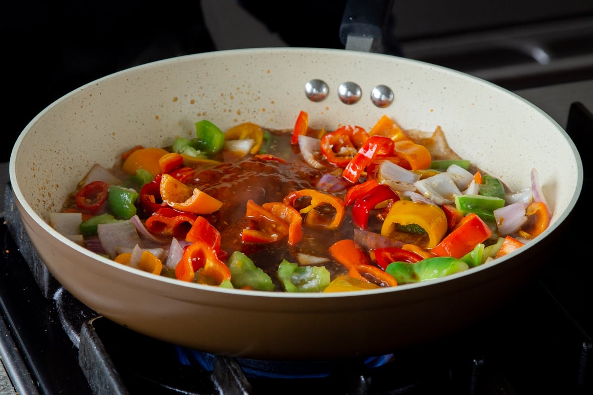 peppers and onions in the frying pan with gochujang and other sauces added, before mixing