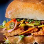 close-up of a gochujang sandwich with pickled veggies on a wooden cutting board