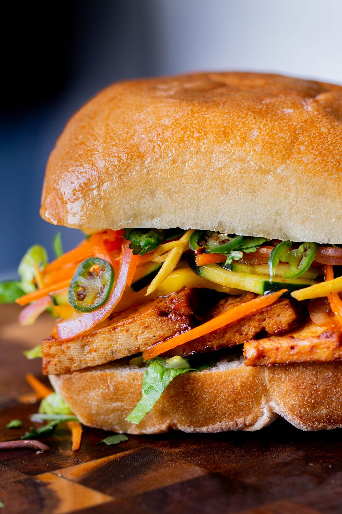 close-up of a gochujang sandwich with pickled veggies on a wooden cutting board