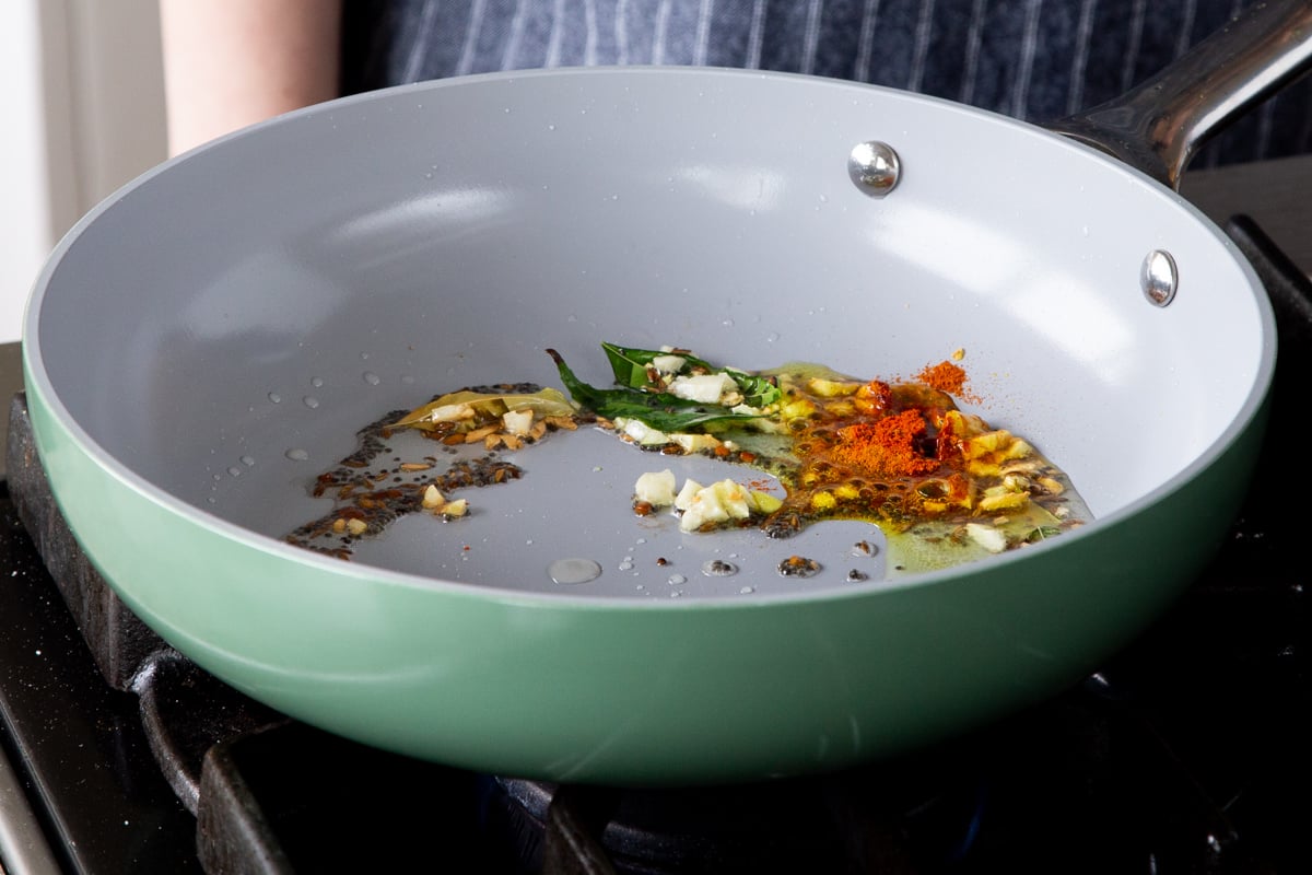 adding powdered spices to the pan of tempering