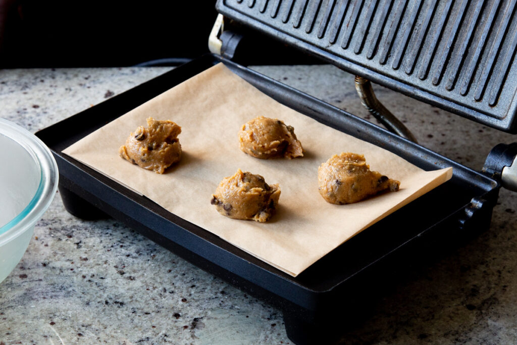 scoops of cookie dough on the parchment paper in the panini press