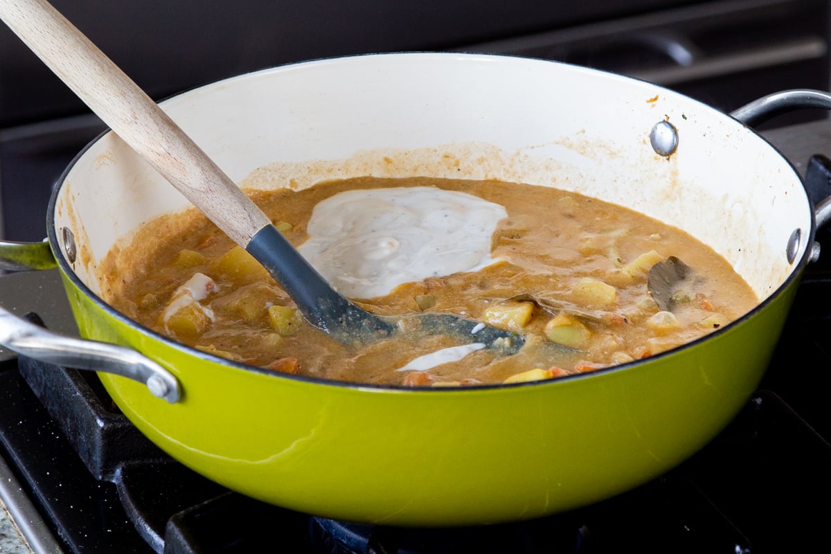 adding vegan yogurt to the cooked potato soup in the pan