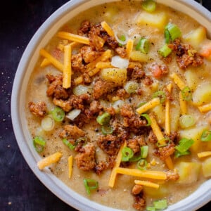 bowl of smoky vegan potato soup topped with tofu crumbles, green onions, and vegan cheese