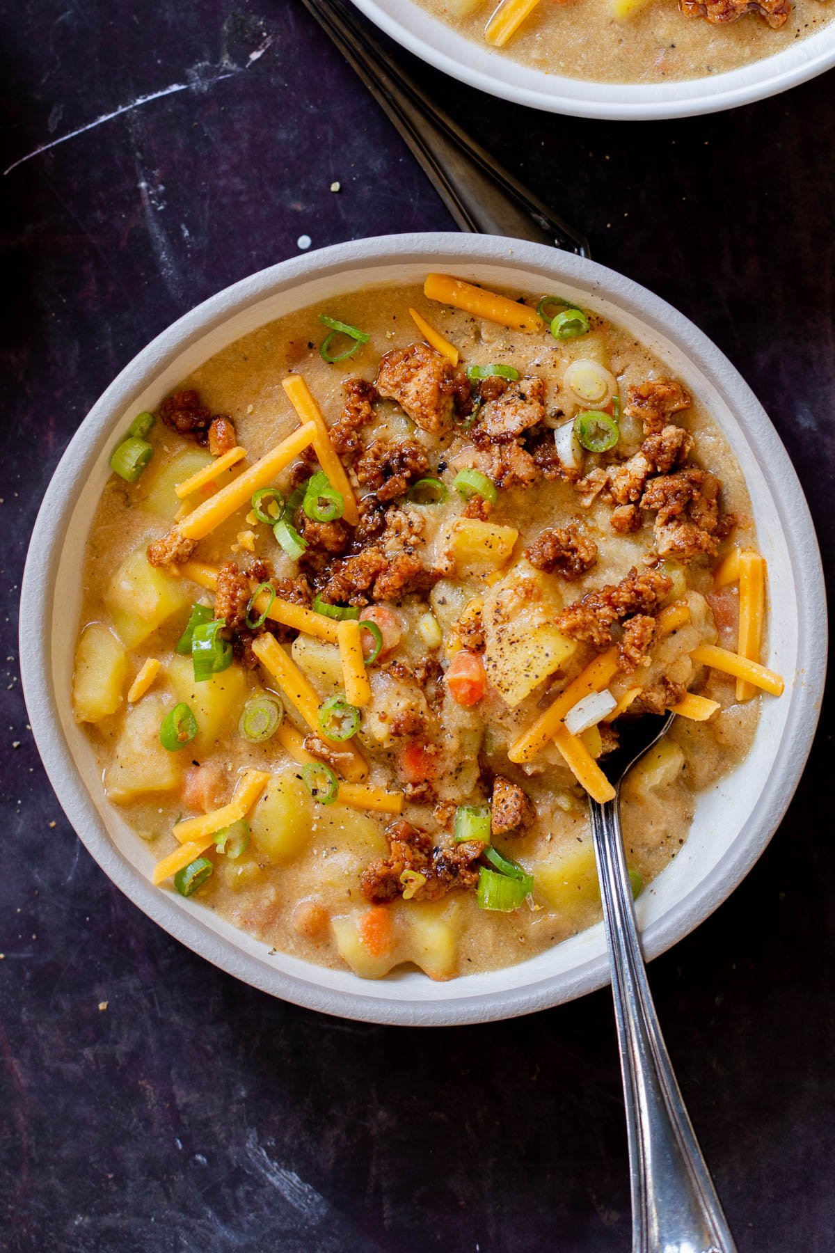bowl of smoky vegan potato soup topped with tofu crumbles, green onions, and vegan cheese