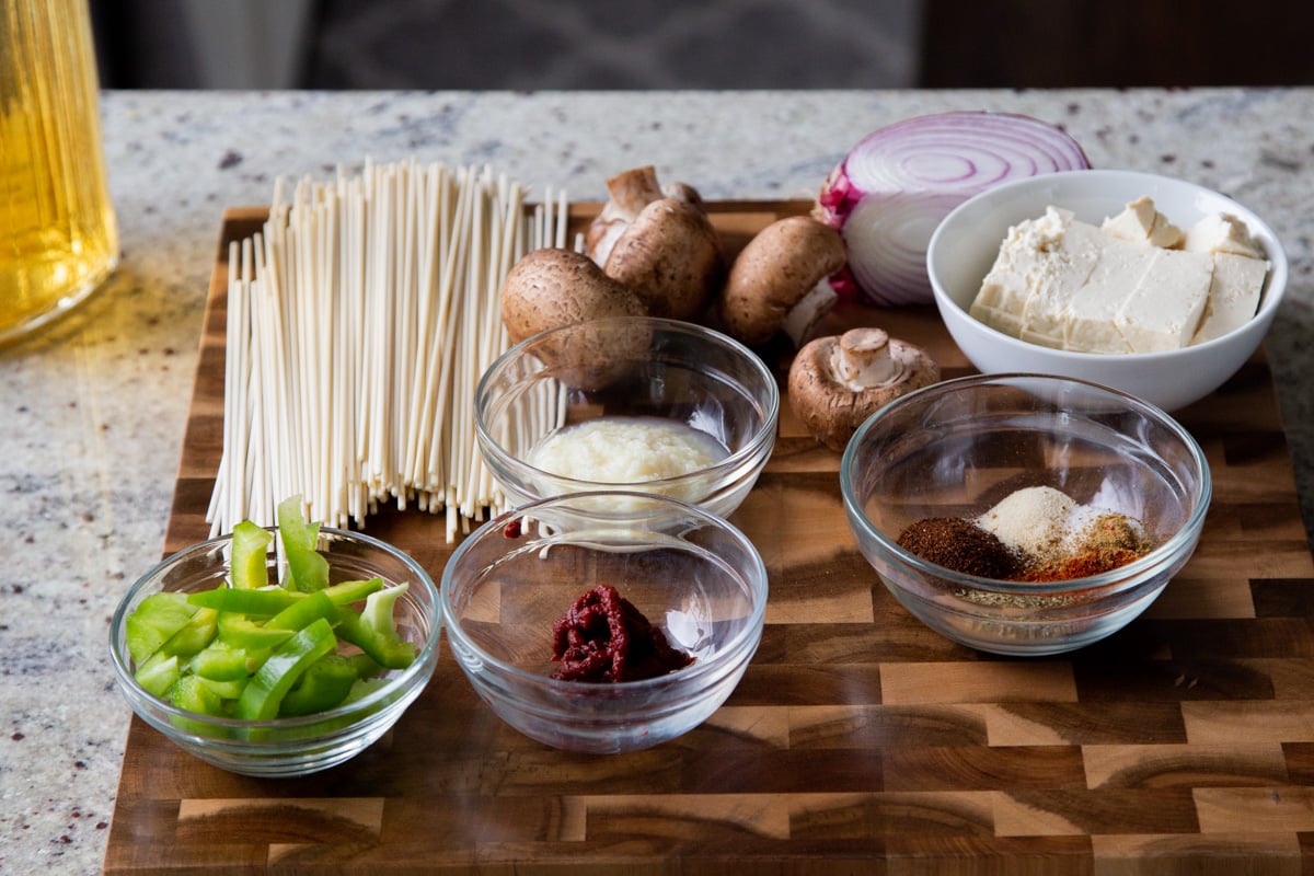 ramen, veggies, and birria broth ingredients on a wooden cutting board