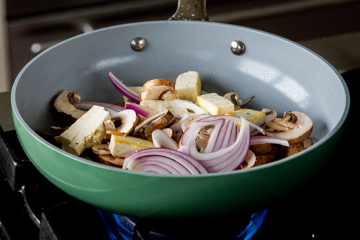 adding mushrooms and onions to the frying pan with the tofu