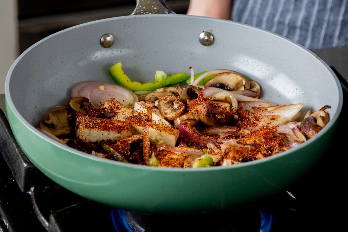 adding spices to the pan of tofu and veggies