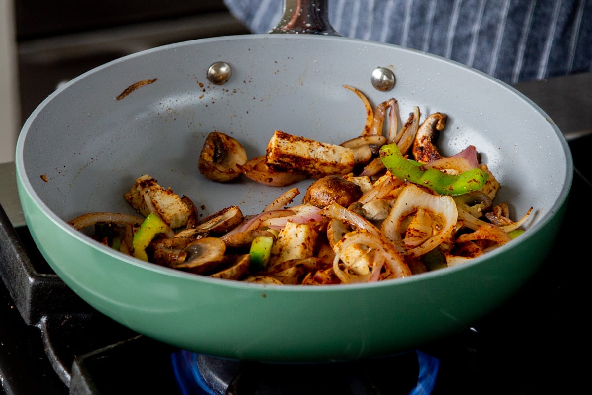 tofu, peppers, and onions int he pan after mixing in the spices
