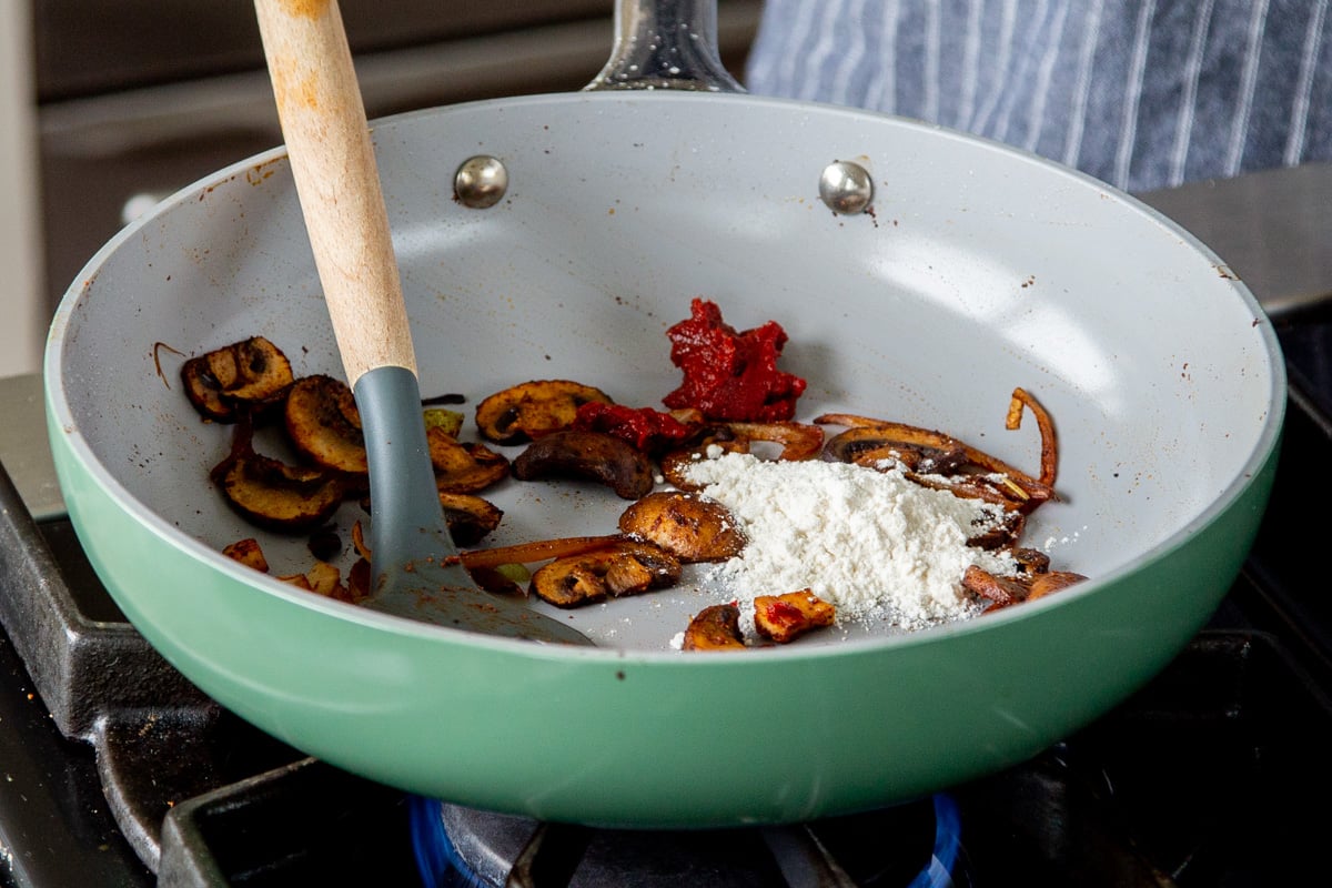 adding flour and tomato paste to the pan of mushrooms and tofu