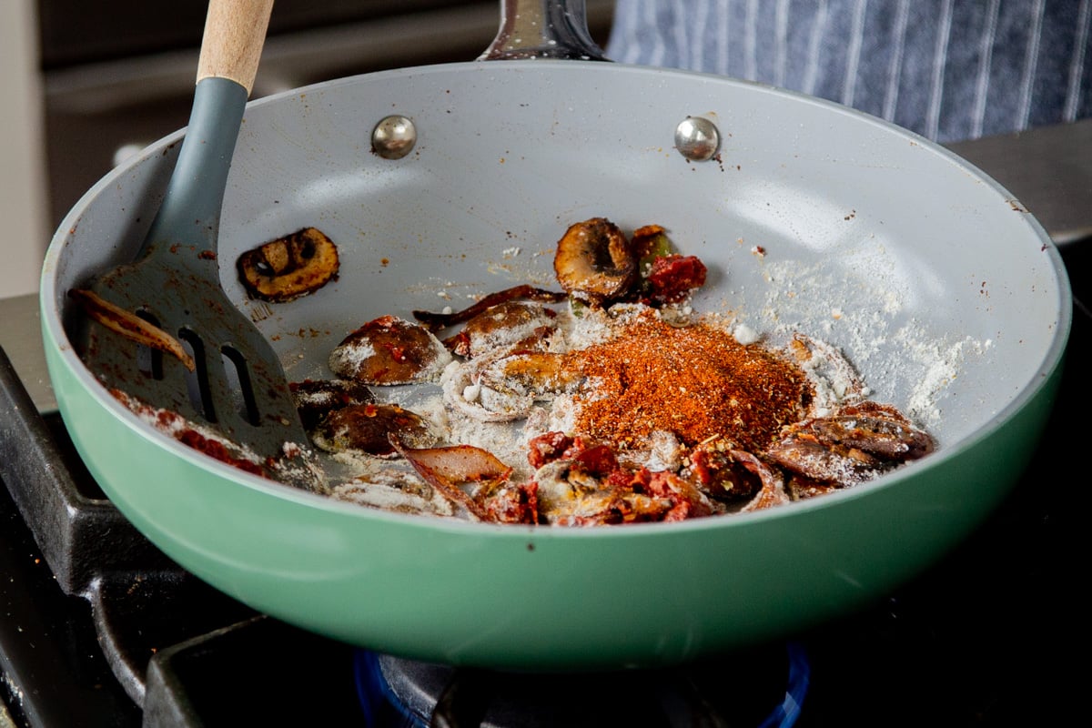 adding spices to the pan of mushrooms, tofu, and tomato paste