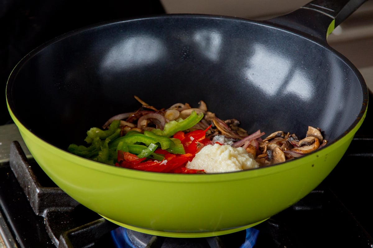 adding bell peppers and ginger-garlic paste to the wok with the cooked mushrooms