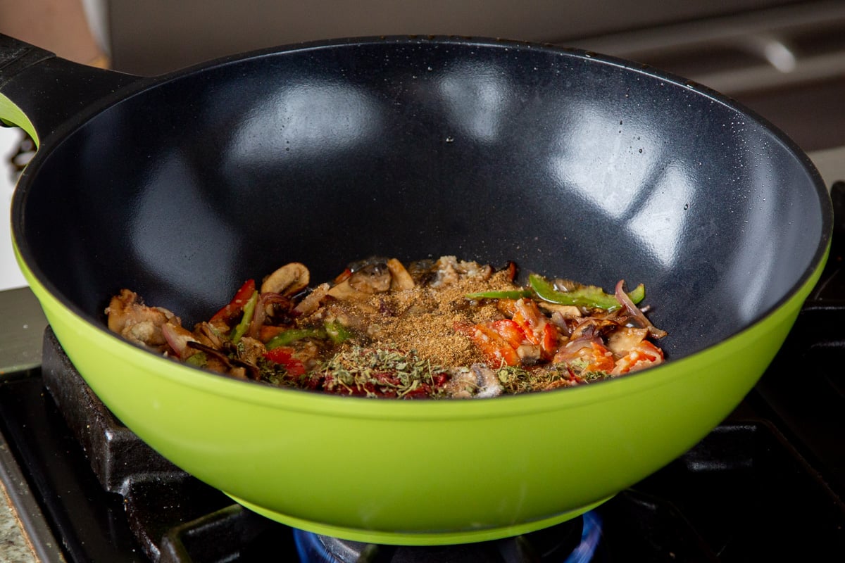 adding spices to the wok of cooked mushrooms and peppers