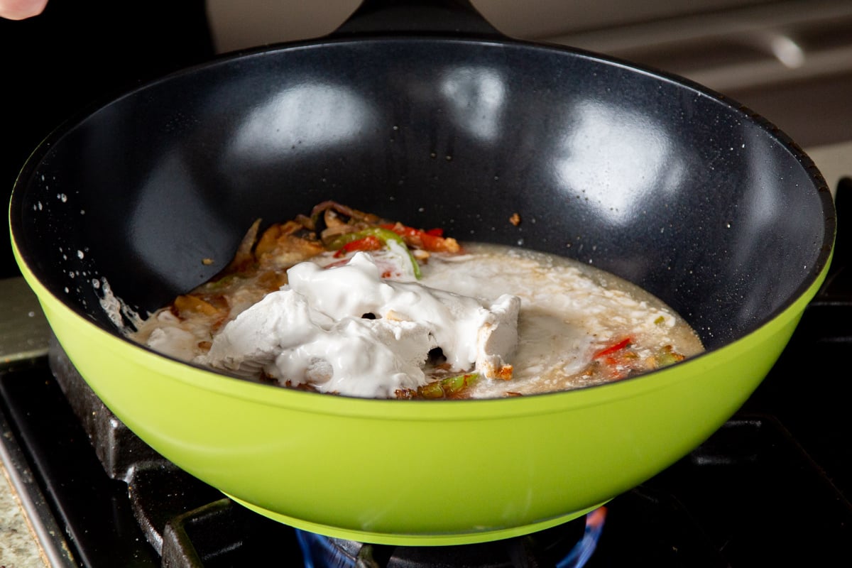 adding coconut milk to the wok with the veggies and spices