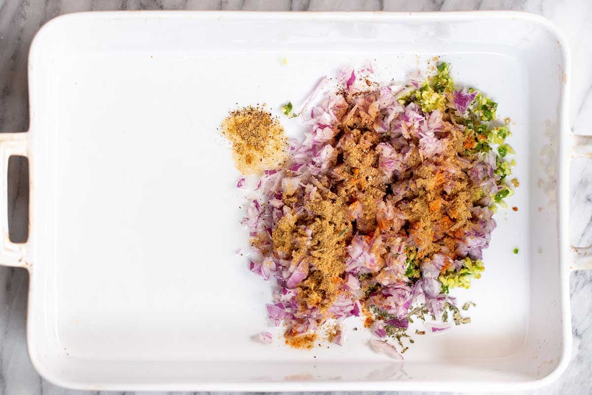aromatics and spices mixed together in half of a baking pan