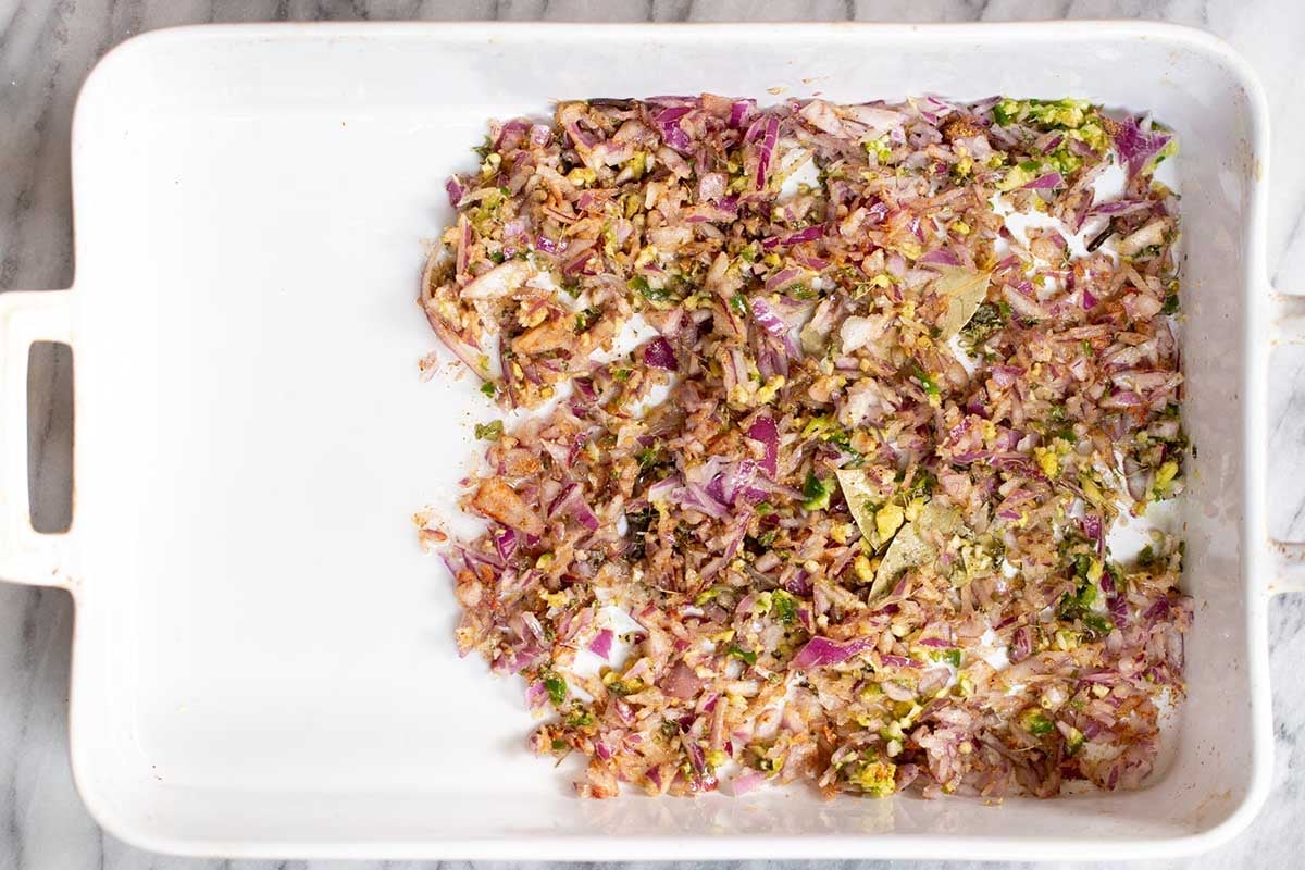 aromatics and spices mixed together in half of a baking pan, after spreading them out