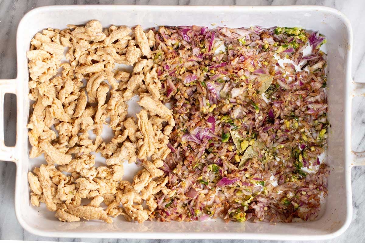 baking pan with soy curls on one half and aromatics and spices on the other half, before baking