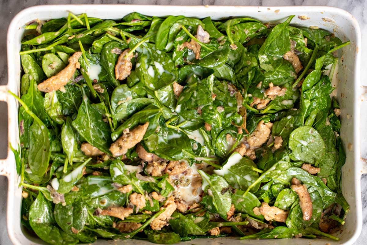 adding spinach to the pan of curry, before baking