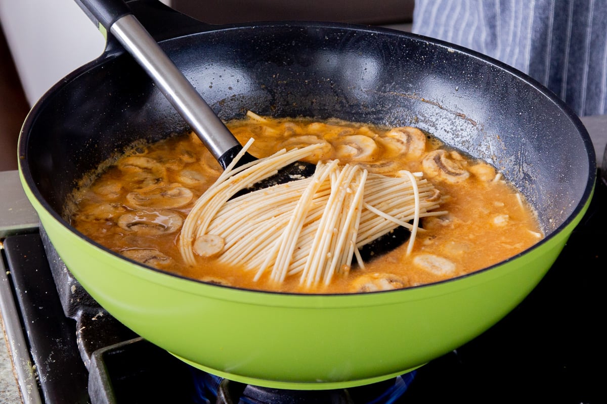 adding ramen noodles to the spicy peanut broth